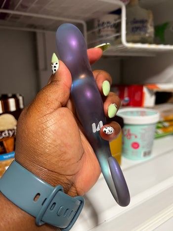 Hand holding frosted glass dildo in front of freezer