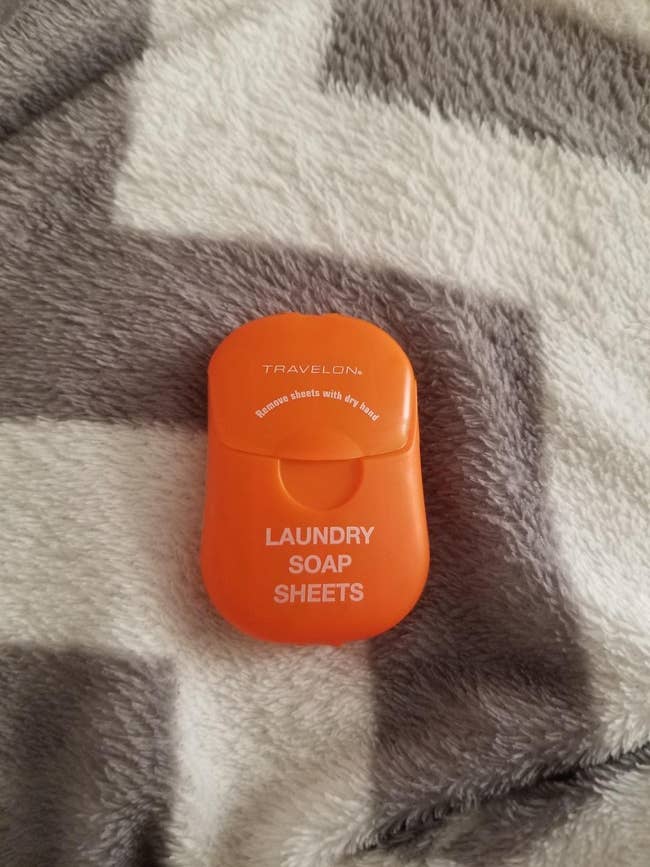 reviewer showing the orange container of the laundry soap sheets on a blanket