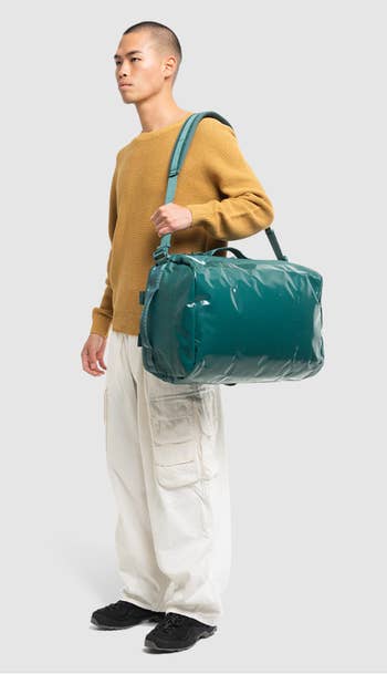 a model wearing the bag in dark blue on their shoulder like a duffel bag 