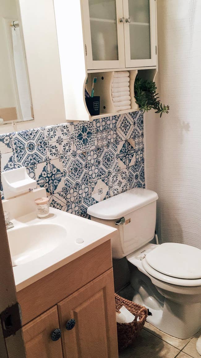 same tile peel-and-stick wallpaper in blue and white pattern above reviewer's bathroom sink and toilet