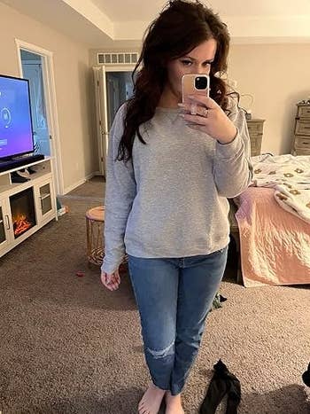 grey sweatshirt and jeans. Room disposable with a TV, fireplace, and furniture successful the background