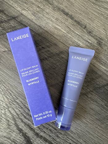 Laneige Lip Glowy Balm successful Blueberry flavor, displayed with its container connected a wood surface