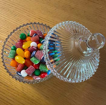 reviewer's overhead photo of the glass candy dish filled with an assortment of colorful candy, with the glass cover leaning against the side