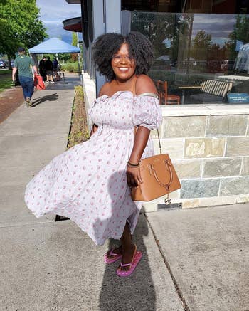 reviewer in a puff-sleeved, floral dress with a handbag, posing outdoors