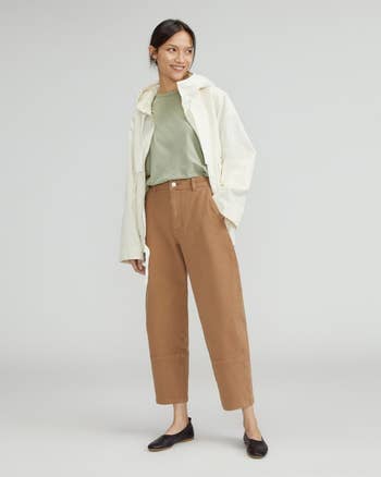 another model wearing the toasted coconut pants with a green tee, cream jacket, and black flats