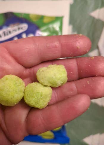 Hand holding 3  round, greenish  puff snacks with a snack container  disposable   successful  the background