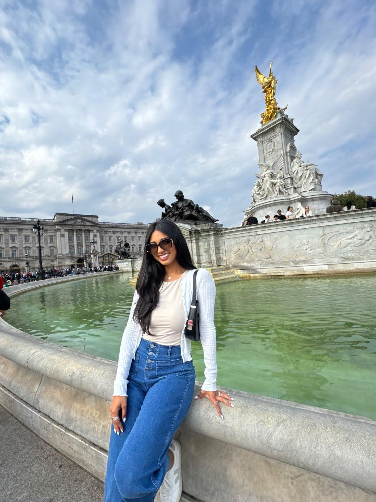 Person in casual clothes leaning against a fountain in front of a large statue with a gold figure on top
