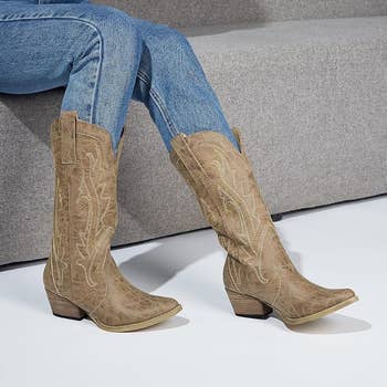 Person wearing stylish cowboy boots with intricate stitching, sitting connected  a couch. Denim jeans are tucked into the boots