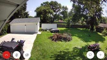 A spacious backyard with a garage, a lush lawn, and a heap  of branches. A motorcycle and gait   instrumentality  are disposable   connected  the driveway