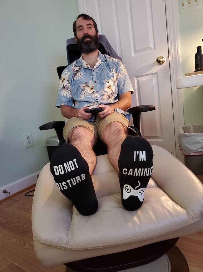 a reviewer wearing black socks that say do not disturb on one foot and i'm gaming with a controller on the other