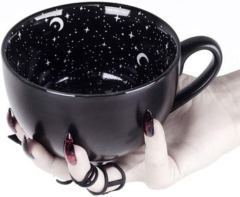 hand holding a large black coffee mug with a celestial print on the inside of the mug