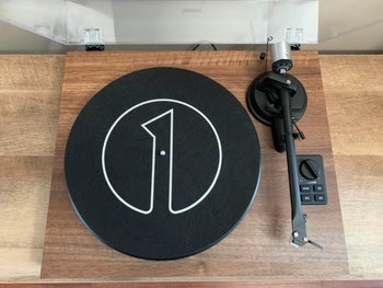 Reviewer image of close up of record player with labels over buttons and single black dial on top o