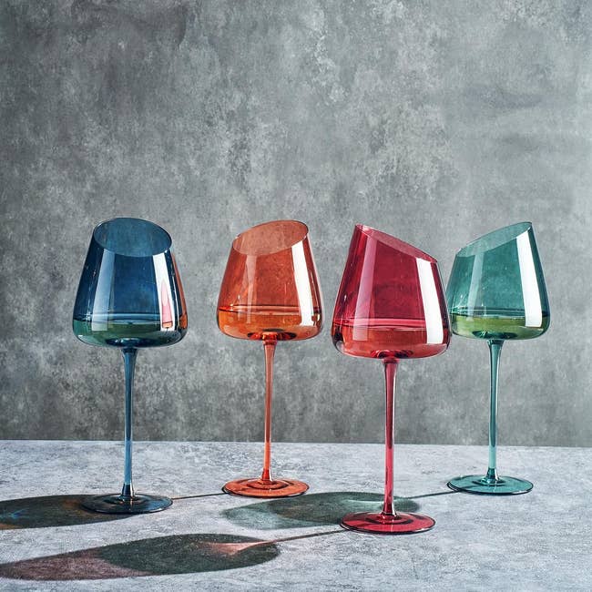 Four modern, asymmetrical vino  glasses successful  varied designs and hues are displayed connected  a textured surface. Ideal for originative  eating  settings
