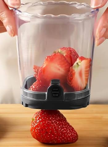 Strawberries being sliced with a hand-held kitchen gadget on a wooden surface
