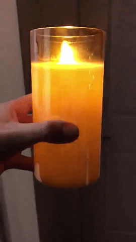 A flickering lit candle with a goldish transparent glass holder in reviewer's hand 