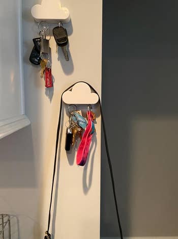 two cloud shaped key holders on a wall, one with a purse strung over it