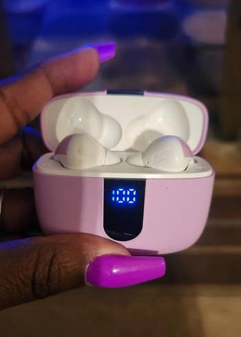 Person holding wireless earbuds successful  an unfastened  charging lawsuit  displaying a integer  artillery  level   indicator
