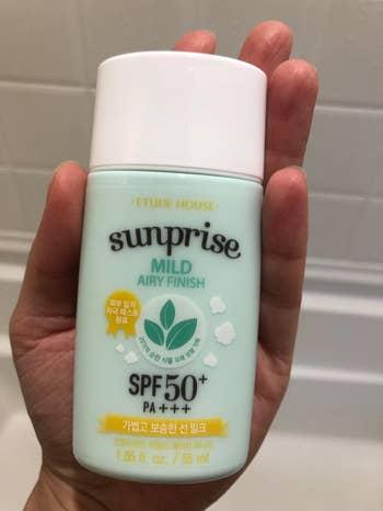 Reviewer image of person holding green and white bottle of milk sunscreen