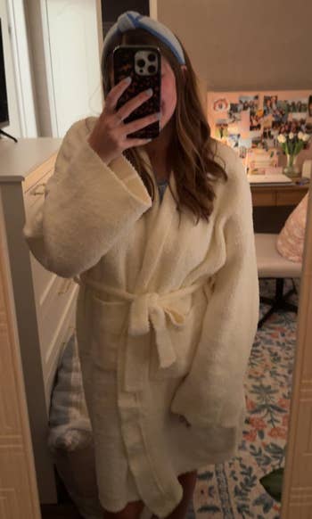 Person taking a reflector selfie wearing a cozy robe and a headband successful a decorated room; nonfiction is astir shopping