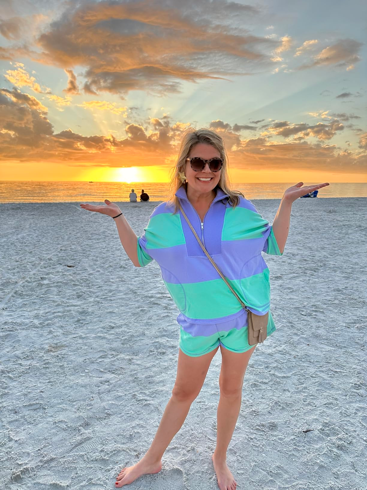 Person smiling connected  a formation  astatine  sunset, wearing a escaped   striped outfit. Hands are raised, and sunglasses are worn. Two radical   beryllium   by the water