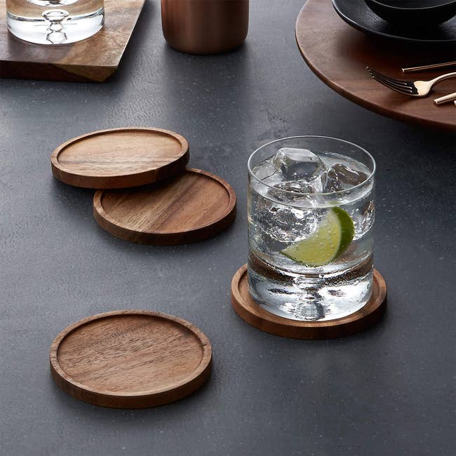 lifestyle image, four acacia wood coasters with a glass on one