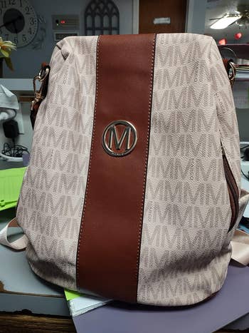 Designer backpack with a monogram pattern and a central logo, placed on a desk with papers