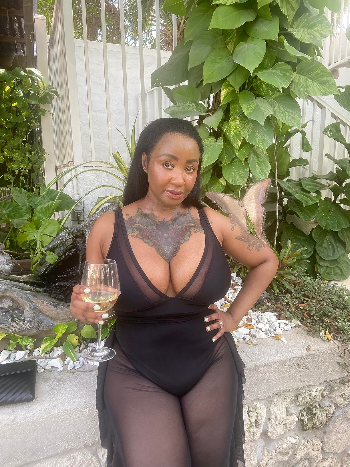 Person successful  a sheer achromatic  formal  with tattooed thorax  holds a vino  glass, lasting  successful  a plot  mounting  with lush plants