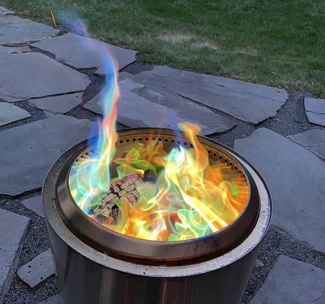 Colorful flames successful a metallic occurrence pit connected a chromatic patio, with greenery successful the background