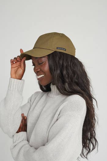 Person successful  a sweater wearing a casual shot   cap, tilting it somewhat  portion    smiling. The headdress  has a tiny  logo tag