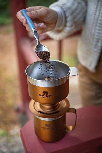Person pouring ground coffee into a portable camping coffee maker