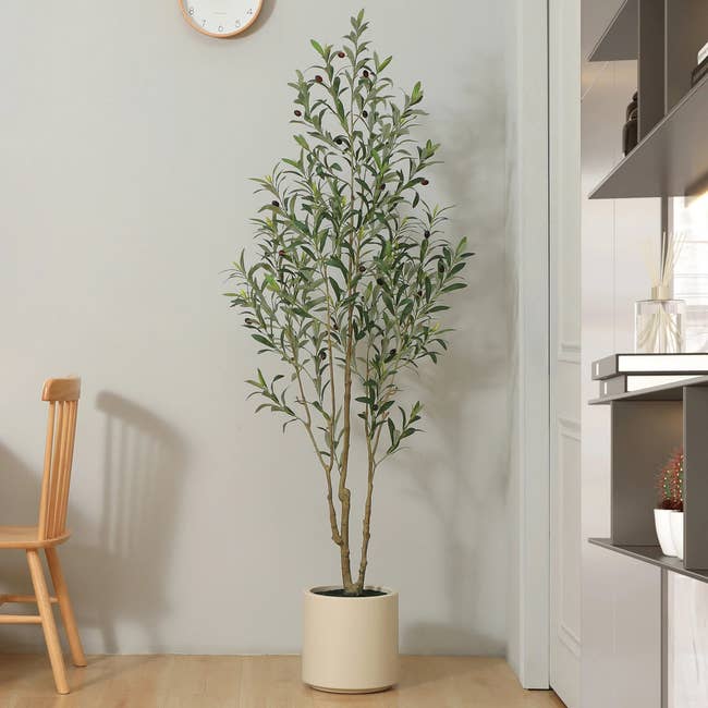 A tall artificial plant in a pot placed in a modern minimalist room next to a wooden chair