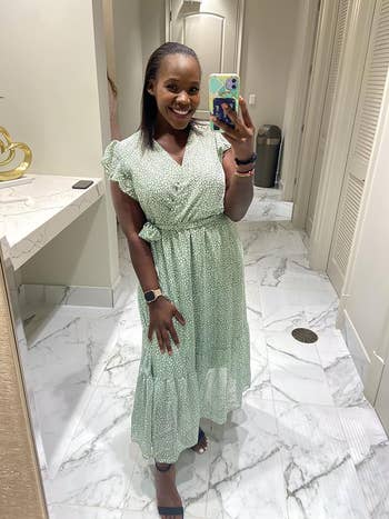 Woman wearing a green patterned dress with puffed sleeves taking a mirror selfie