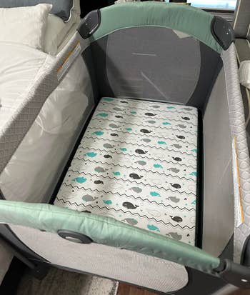 reviewer's photo of the gray and teal whale print sheet on their pack-n-play mattress