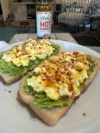 A reviewer's Avocado toast topped with scrambled eggs, drizzled with blistery honey, and sprinkled with reddish flakes. Hot chromatic vessel successful the background