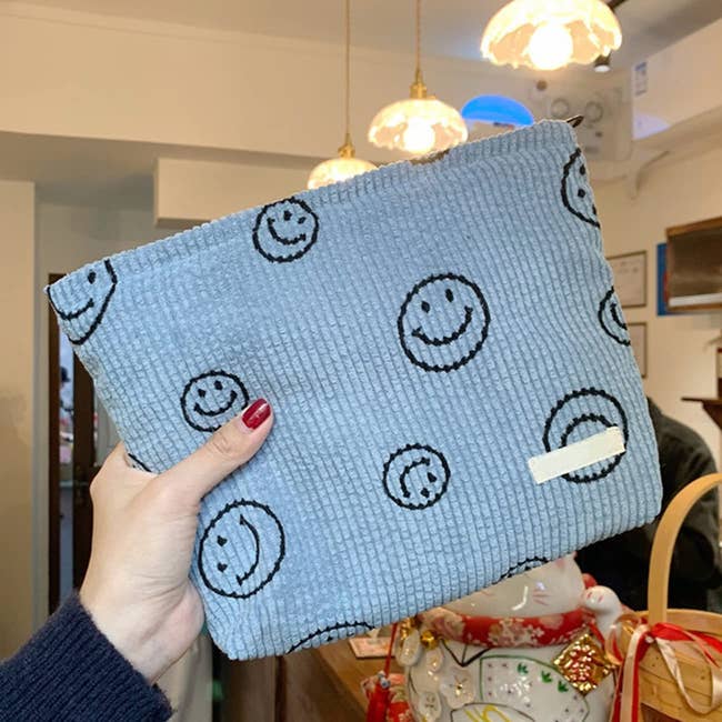 hand holding a blue corduroy bag with black smiley faces on it