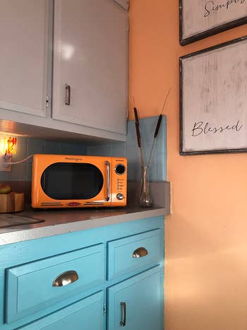 A retro-style orange microwave on a blue kitchen cabinet with a decorative 