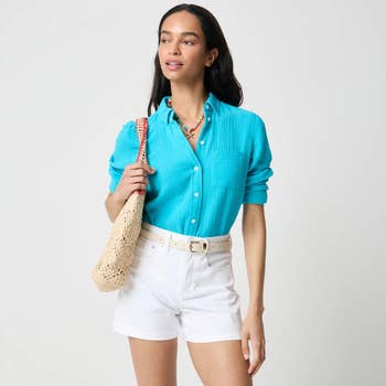 Person wearing a textured shirt, white shorts, and holding a woven bag, styled with a colorful necklace. Suitable for a casual summer look