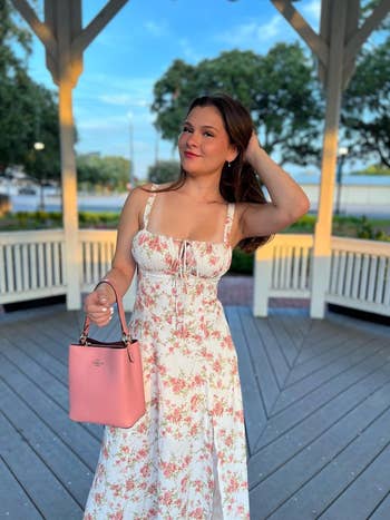 reviewer posing with a floral dress and a pink handbag on a wooden gazebo