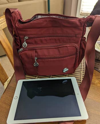 a reviewer photo of the purse in red sitting next to an iPad that fits inside 