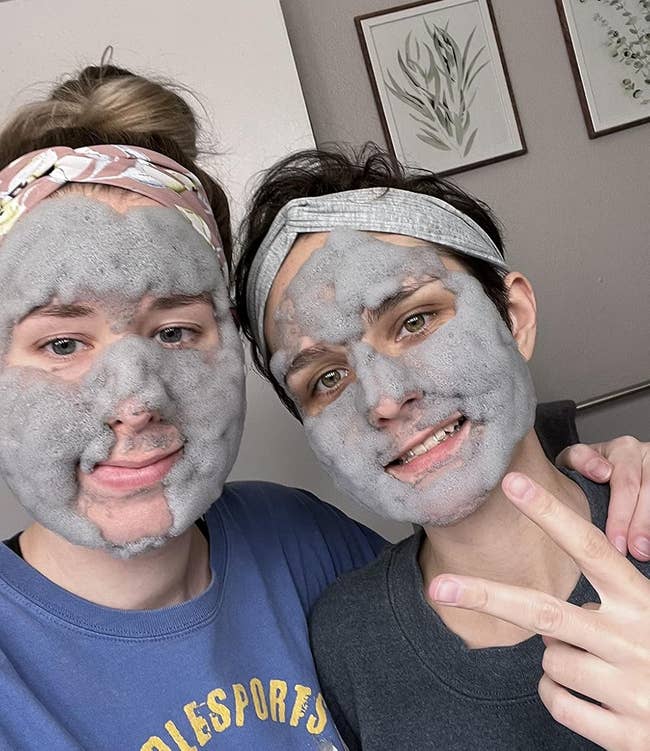 Two people wearing gray bubble face masks and headbands, smiling for the camera in a casual indoor setting