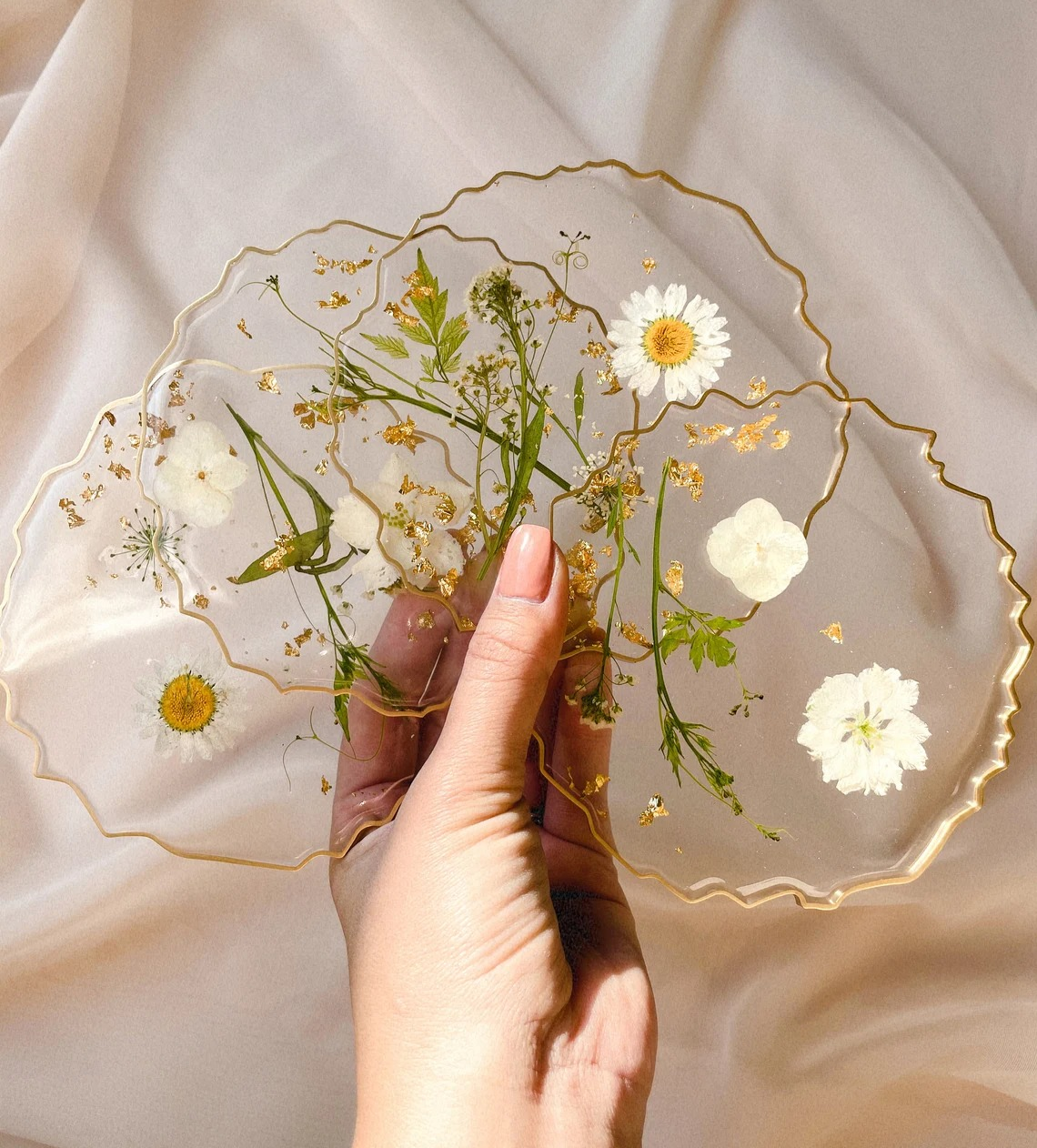 Set of transparent coasters with uneven edged gold rim and white pressed flowers inside 
