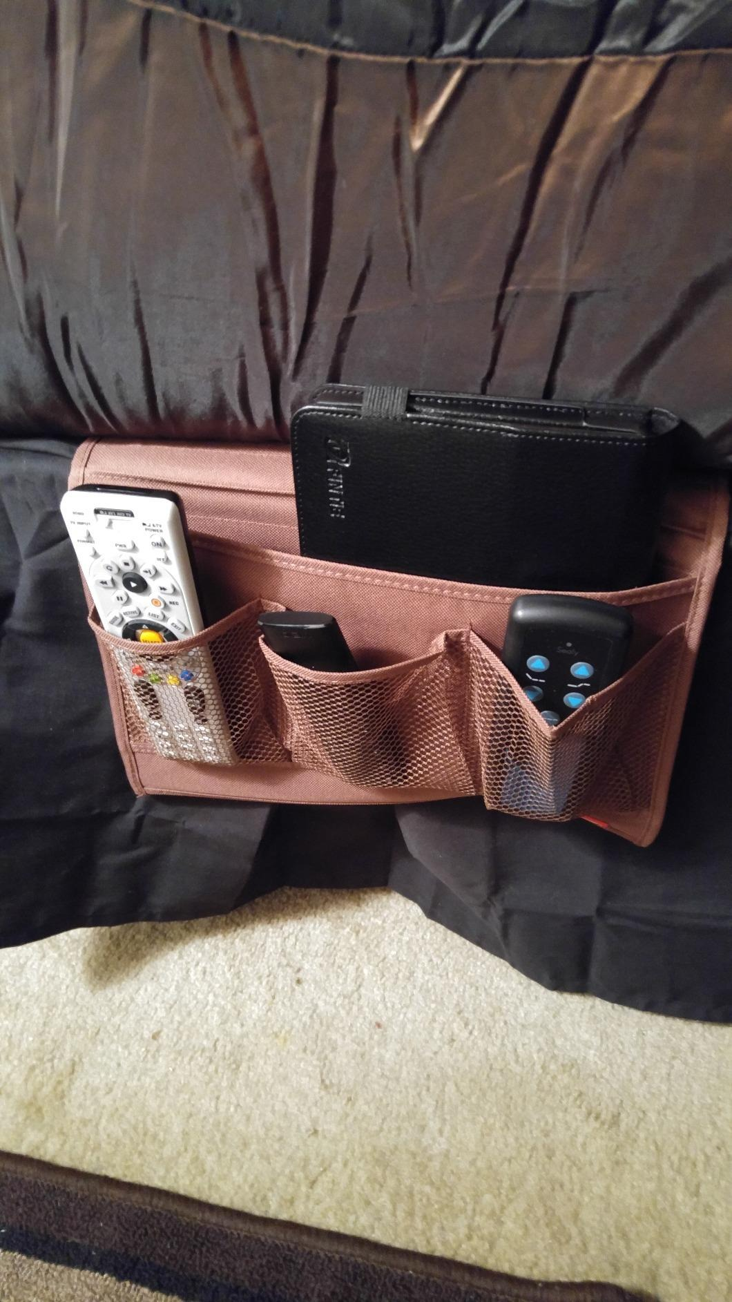 Organizer with pockets holding a tablet, distant    controls, and an physics  instrumentality  connected  the broadside  of a sofa