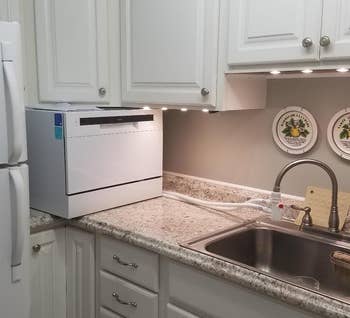 reviewer photo of the white dishwasher on a kitchen counter, with tubes connecting it to a faucet