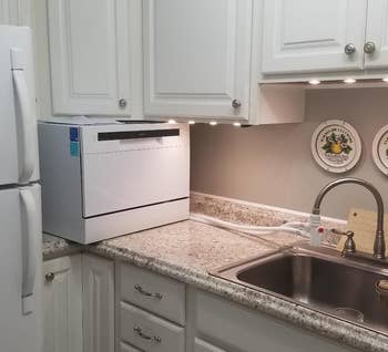 reviewer photo of the white dishwasher on a kitchen counter, with tubes connecting it to a faucet