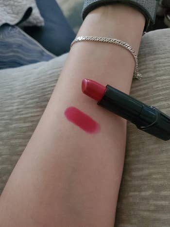 Swatch lipstik pada lengan bawah menunjukkan warna yang semarak di sebelah tabung lipstik; Sempurna untuk artikel belanja kecantikan