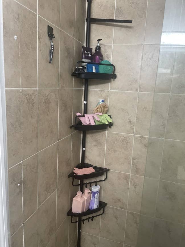 Corner ablution caddy with 3 shelves holding assorted toiletries and cleaning accessories, mounted successful a tiled shower