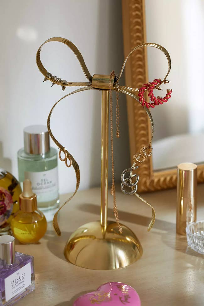 Elegant jewelry stand shaped like a ribbon with a ring and necklace displayed on it, next to perfumes