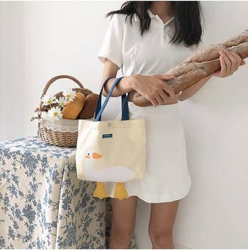 Person successful  a achromatic  outfit holding baguettes adjacent  to a array  with a daisy-filled basket. She's carrying a tote with a duck design