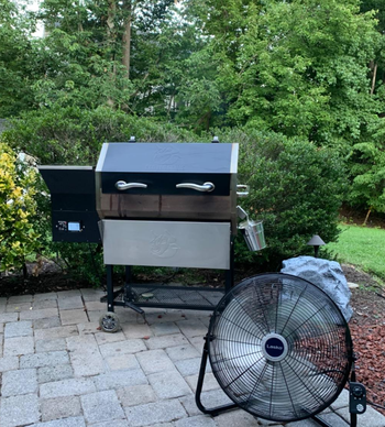 reviewer photo of the black fan on an outdoor patio next to a grill