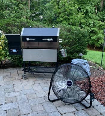 reviewer photo of the black fan on an outdoor patio next to a grill
